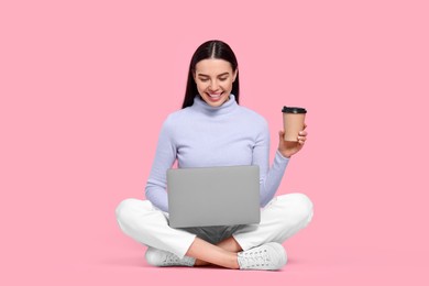 Happy woman with laptop and paper cup on pink background