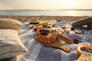 Photo of Different tasty snacks and wine on picnic blanket near river