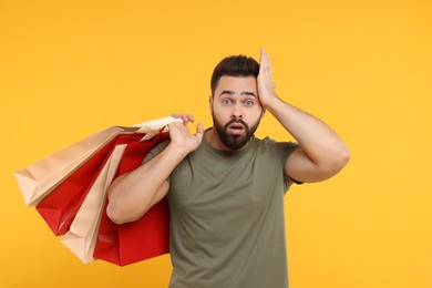 Photo of Shocked man with many paper shopping bags on orange background