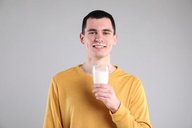 Photo of Happy man with milk mustache holding glass of tasty dairy drink on gray background