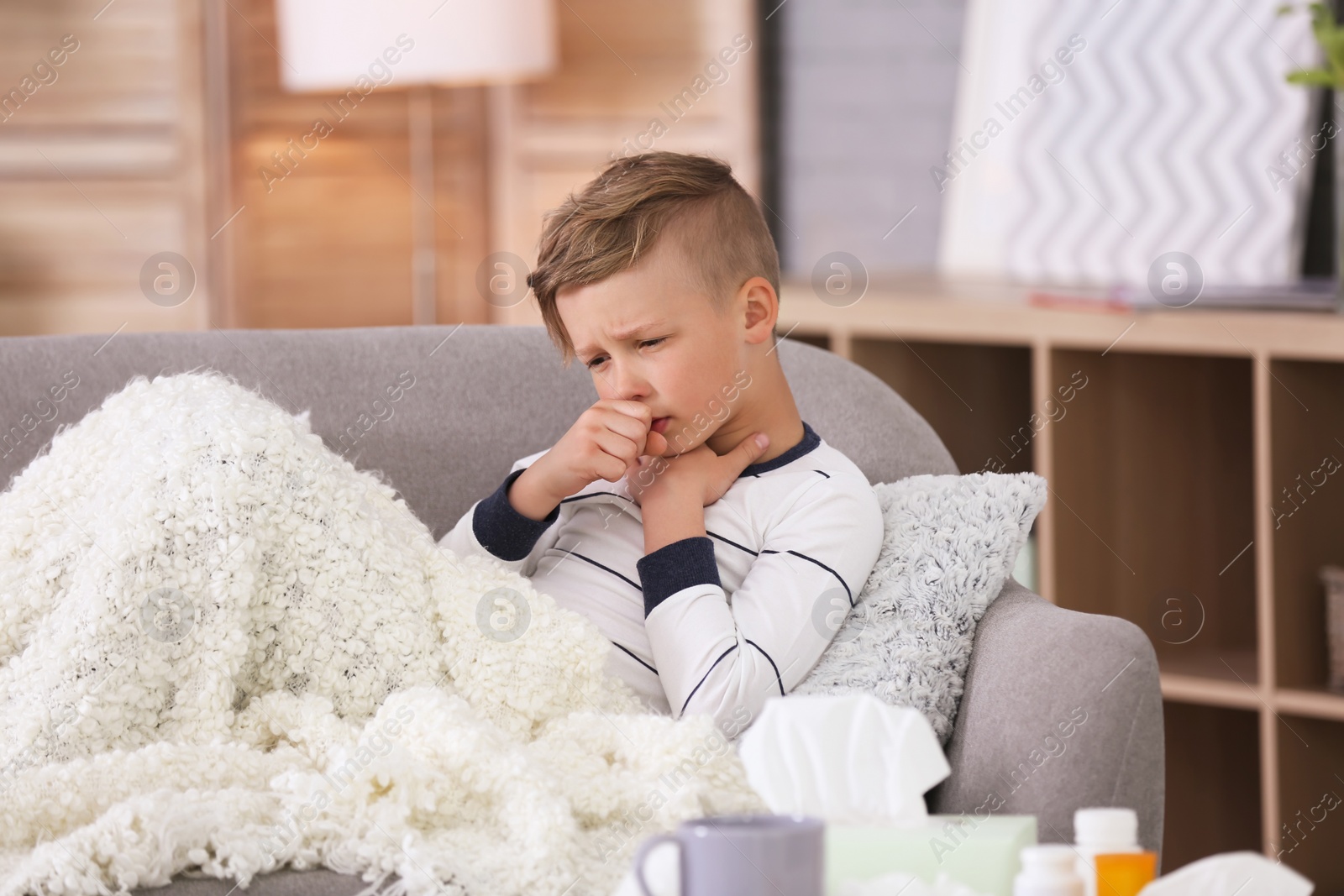 Photo of Little boy with cough suffering from cold on sofa at home