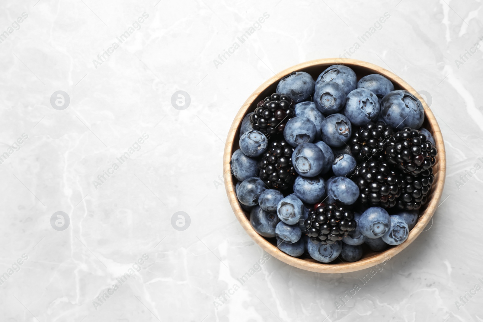 Photo of Blueberries and blackberries on light marble table, top view. Space for text