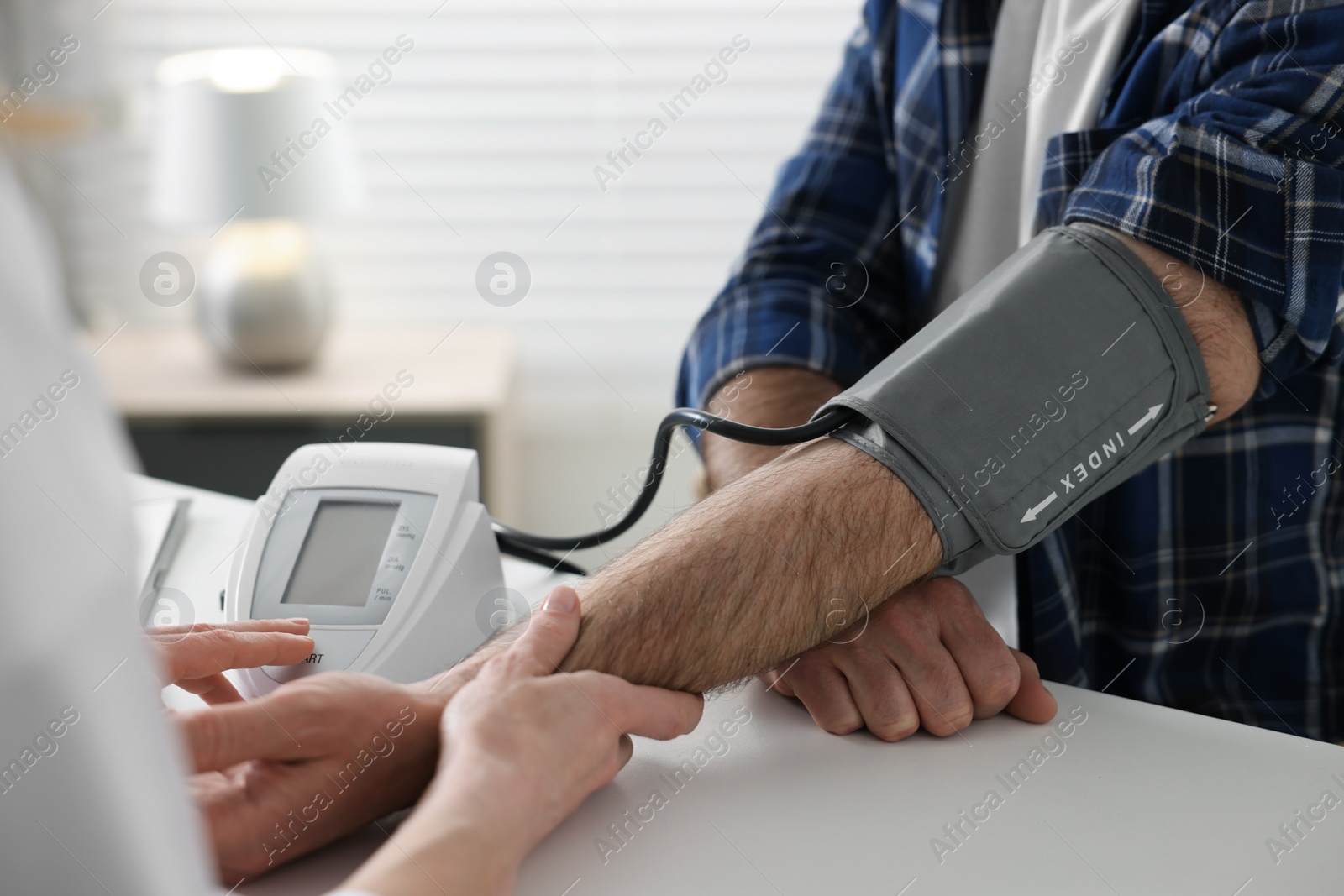 Photo of Doctor measuring blood pressure of man at table indoors, closeup