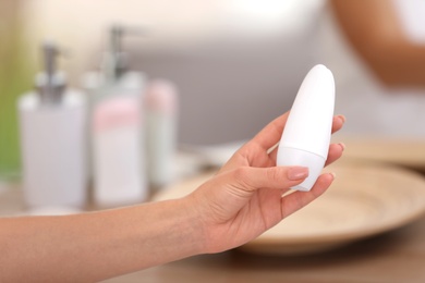 Photo of Young woman holding deodorant in bathroom, closeup