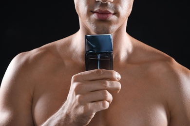 Young man with bottle of perfume on black background, closeup