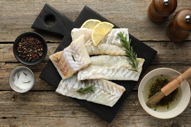 Fresh raw cod fillets, spices and lemon on wooden table, flat lay