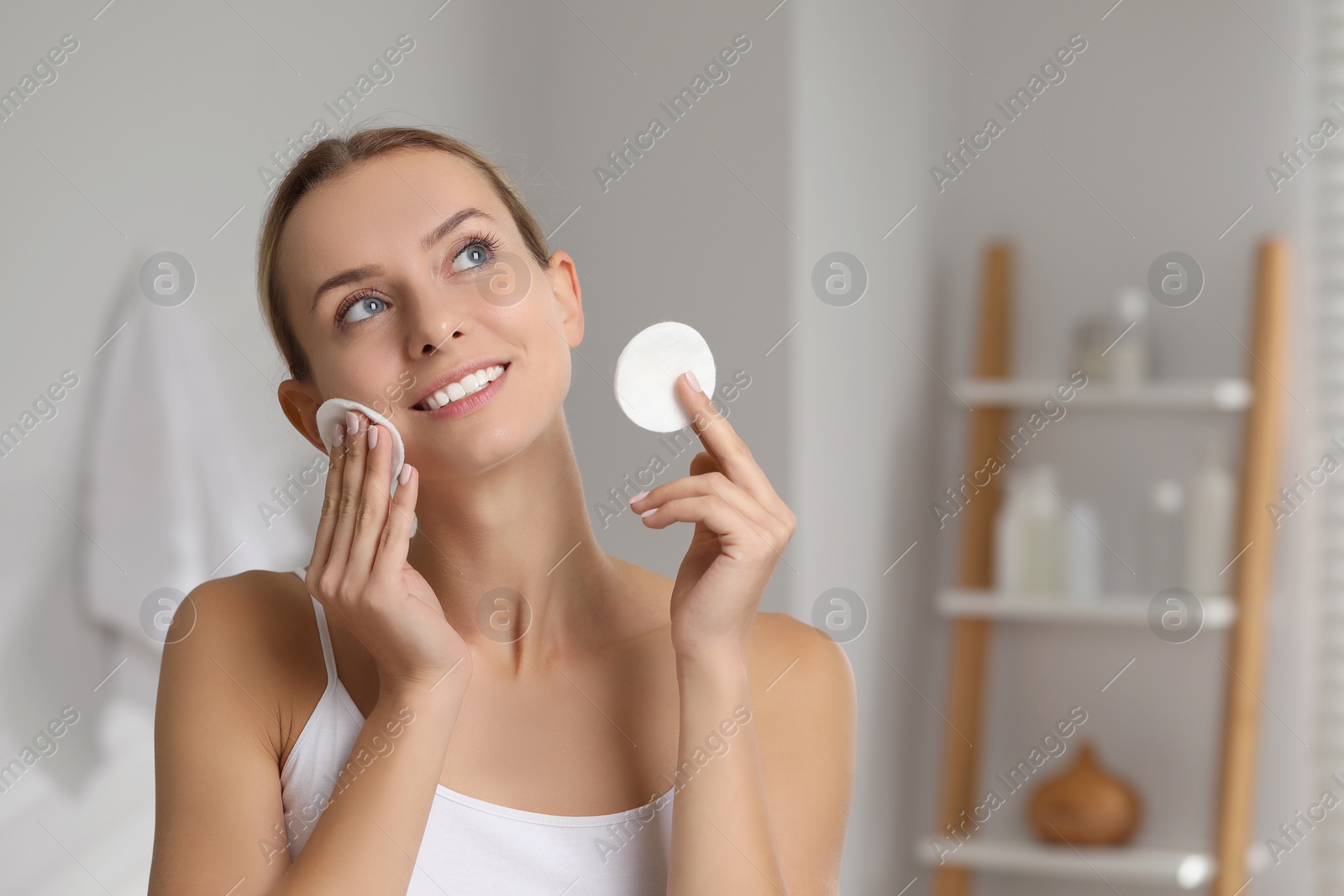 Photo of Smiling woman removing makeup with cotton pads in bathroom