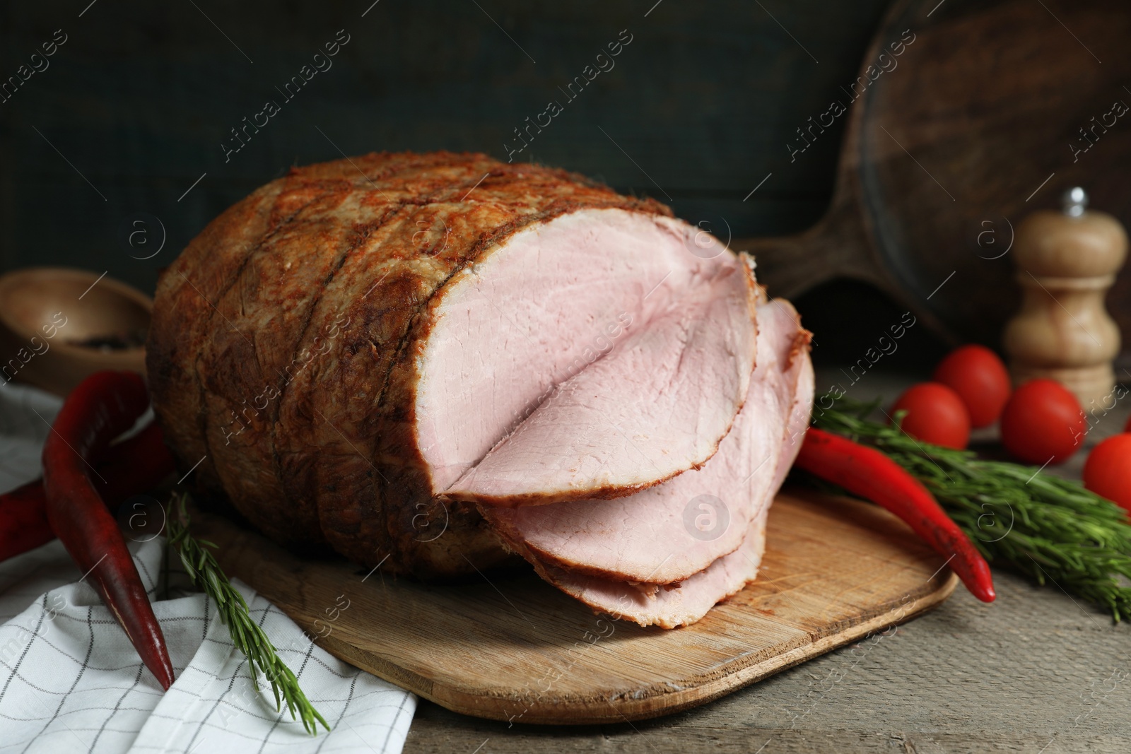 Photo of Delicious baked ham, tomatoes, chili peppers and rosemary on grey wooden table
