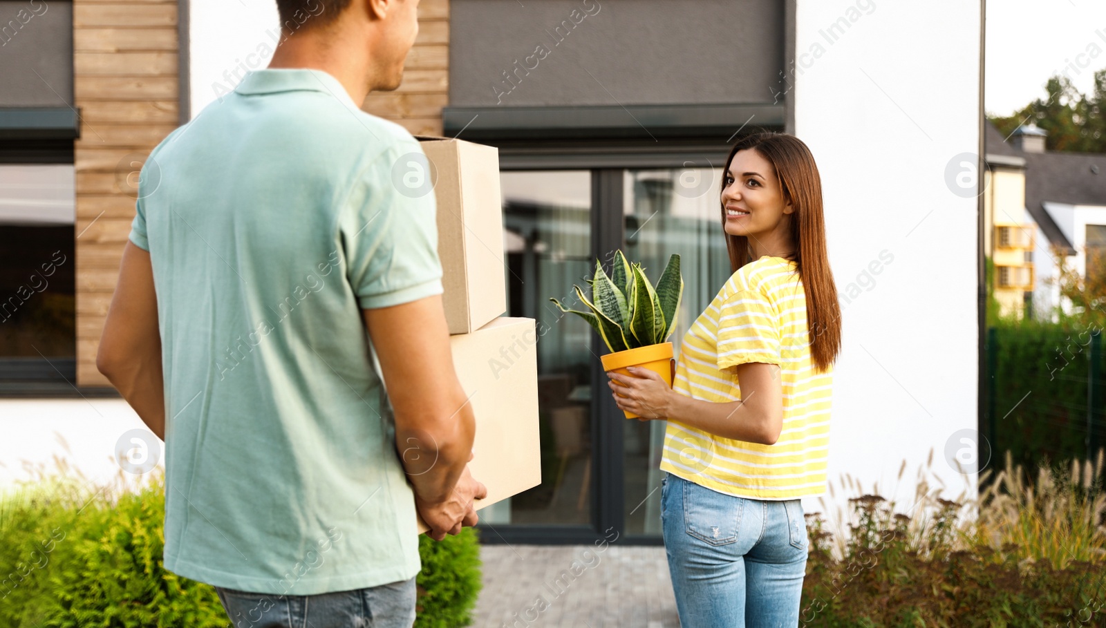 Photo of Couple walking to their new house with moving boxes and household stuff