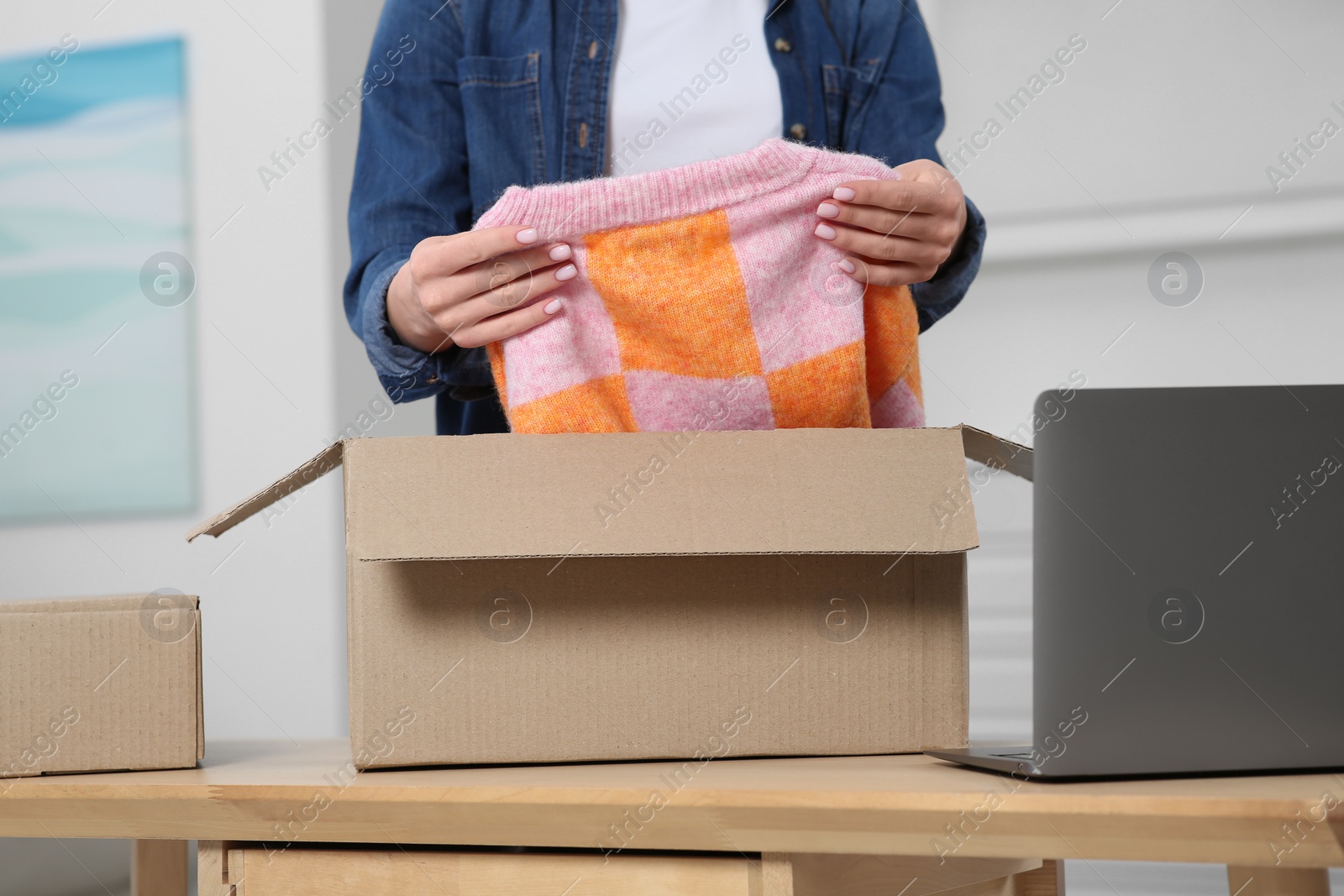 Photo of Woman unpacking parcel at wooden table indoors, closeup. Online store