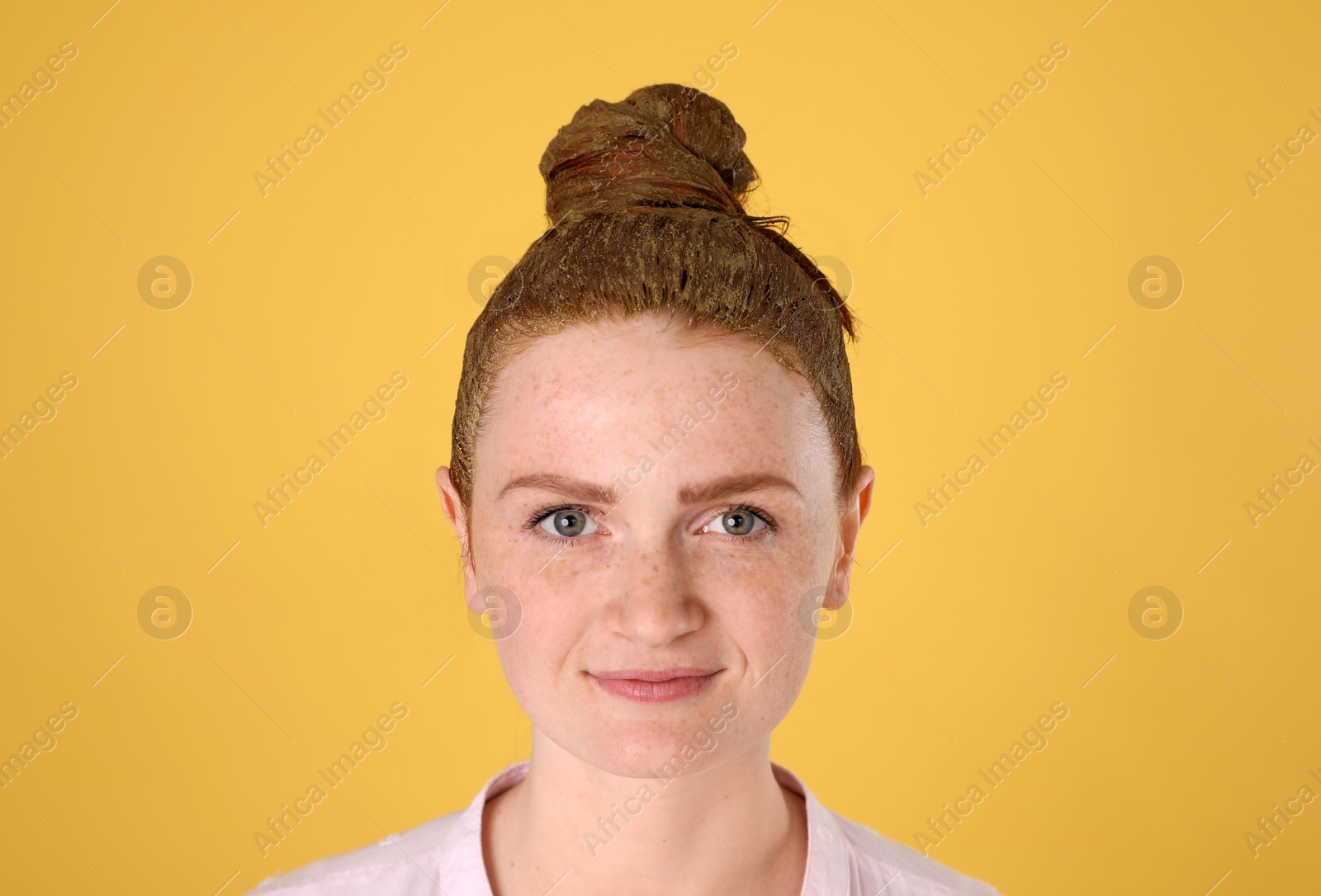 Photo of Young woman dyeing her hair with henna on yellow background