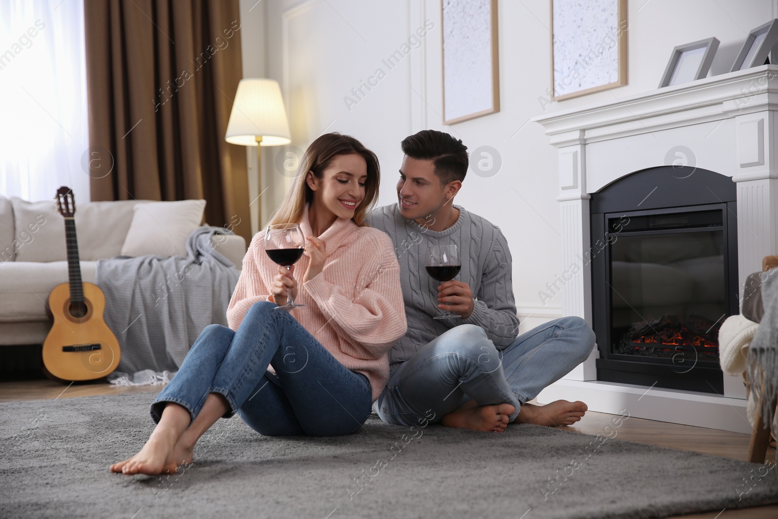 Photo of Happy couple with glasses of wine resting near fireplace at home