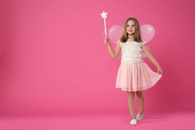 Photo of Cute little girl in fairy costume with wings and magic wand on pink background. Space for text