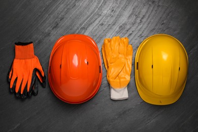 Photo of Hard hats and gloves on black table, flat lay. Safety equipment
