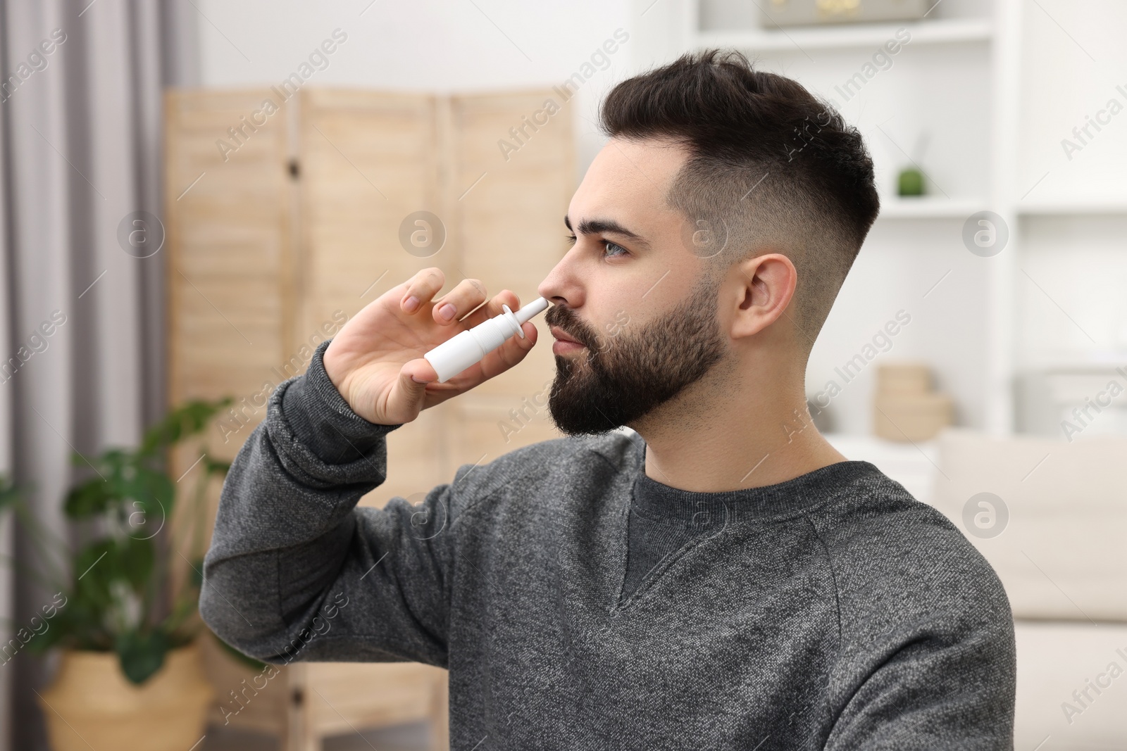 Photo of Medical drops. Young man using nasal spray indoors