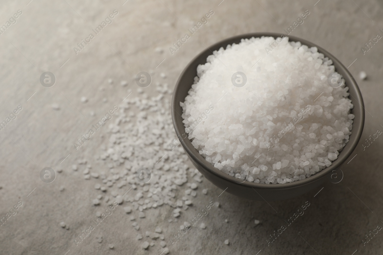 Photo of Natural salt in bowl on grey table, space for text