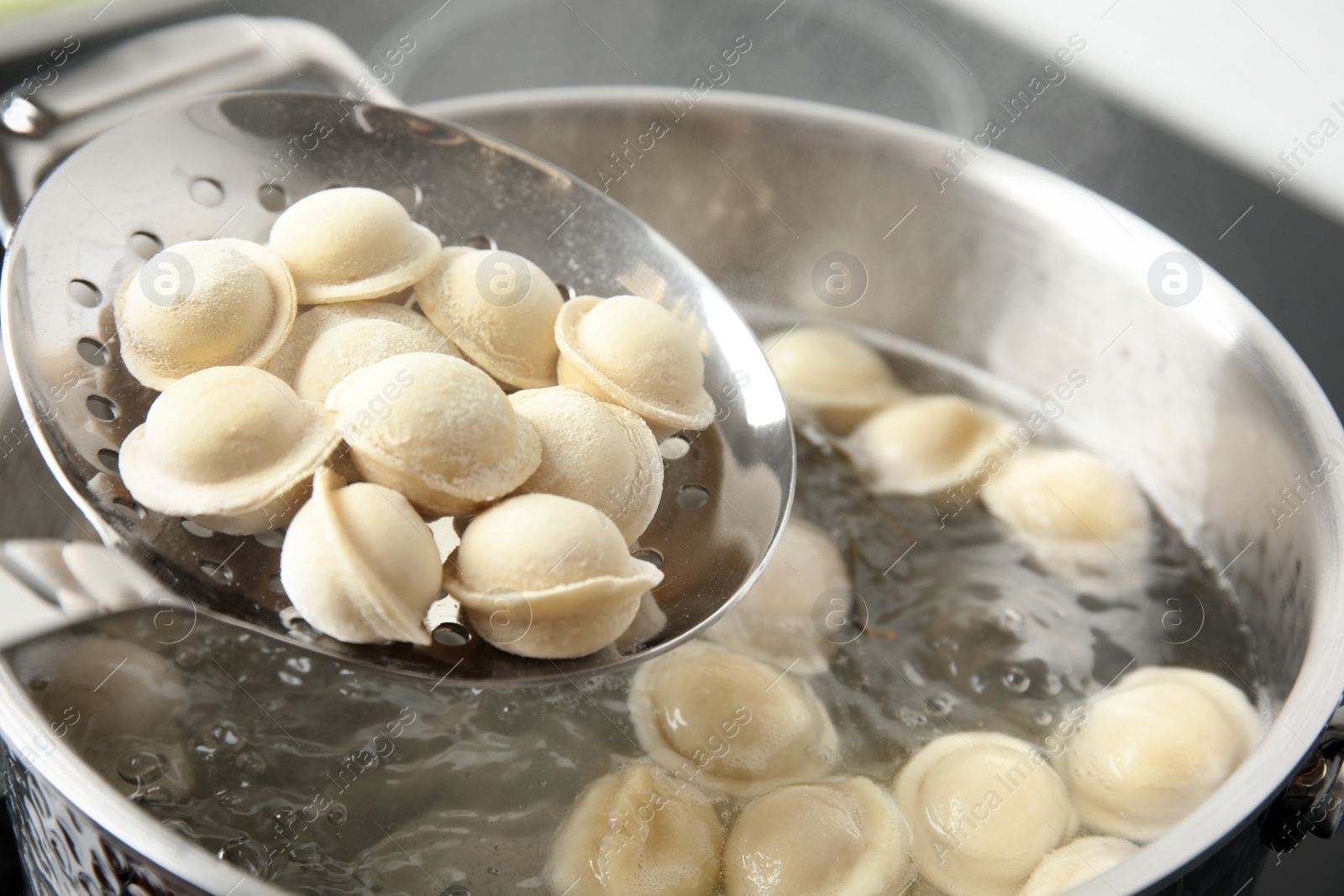 Photo of Closeup of dumplings on skimmer over stewpan with boiling water. Home cooking