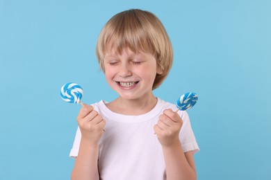 Photo of Happy little boy with bright lollipops on light blue background