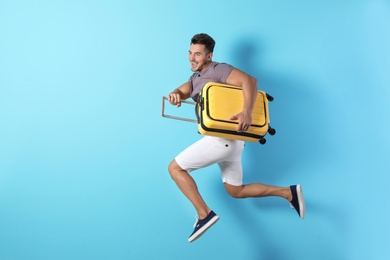 Photo of Young man jumping with suitcase on color background