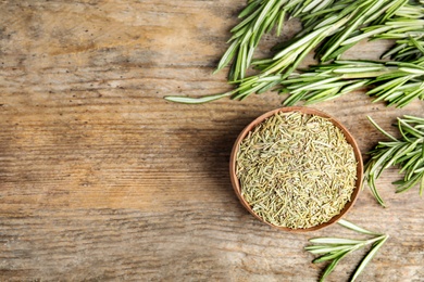 Bowl of dried rosemary and fresh leaves on wooden background, flat lay. Space for text