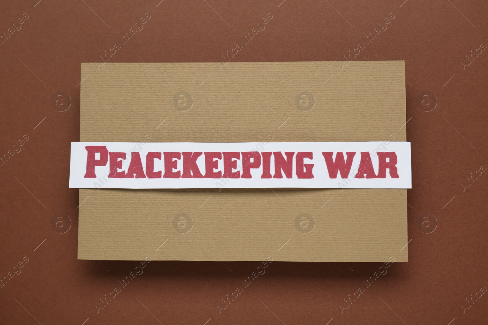 Photo of Paper card with phrase Peacekeeping War on brown background, top view