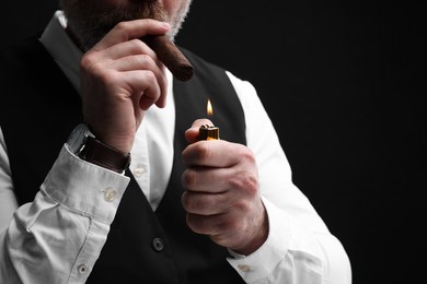 Man lighting cigar on black background, closeup. Space for text