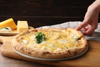 Woman taking piece of delicious cheese pizza at wooden table, closeup