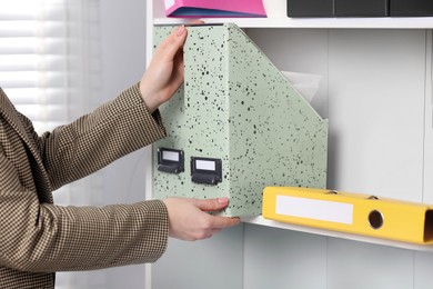 Photo of Woman taking folder with documents from shelf in office, closeup