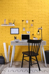 Stylish home office interior with comfortable workplace near yellow brick wall