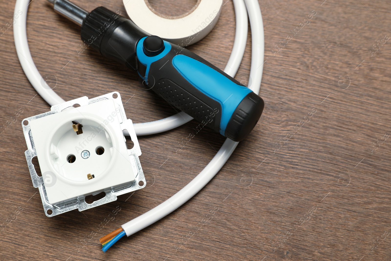 Photo of Screwdriver, cable, insulating tape and power socket on wooden table. Space for text