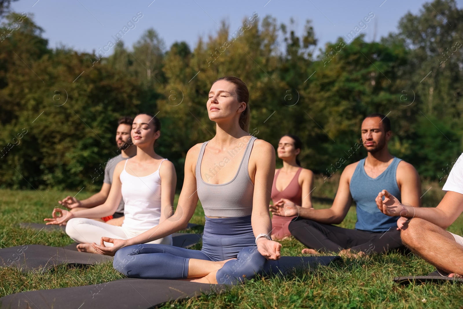 Photo of Group of people practicing yoga on mats outdoors. Lotus pose