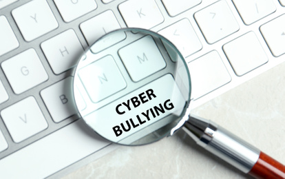 Magnifying glass and computer keyboard with phrase CYBER BULLYING on white button, top view