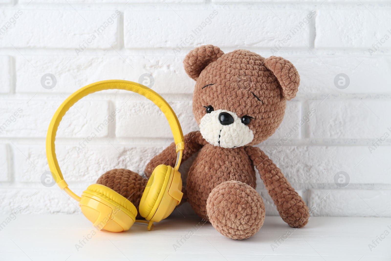 Photo of Baby songs. Toy bear and yellow headphones on white wooden table