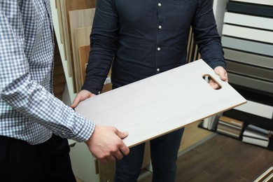 Men holding sample of wooden flooring in shop, closeup