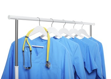 Photo of Light blue medical uniforms and stethoscope on rack against white background