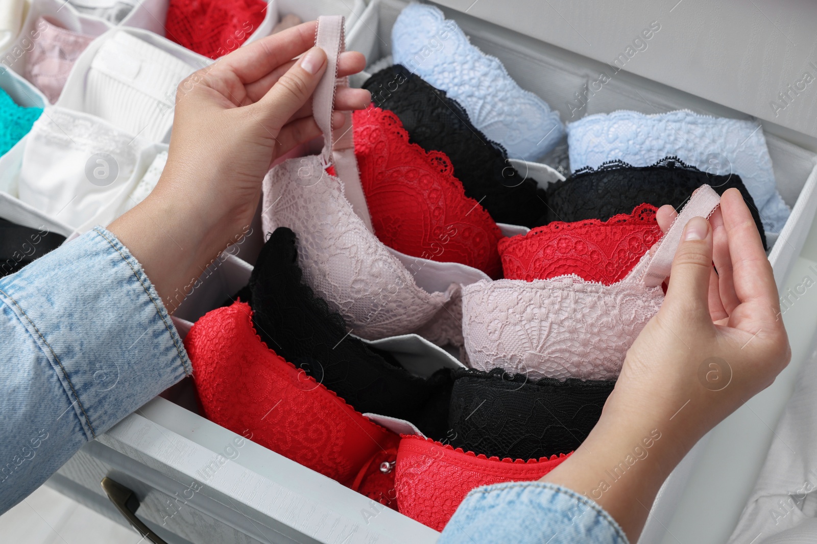 Photo of Woman putting beautiful bra into organizer with underwear in drawer, closeup