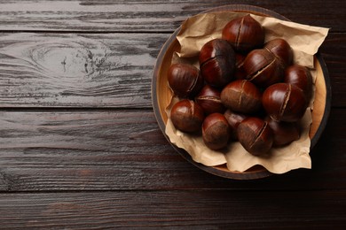 Photo of Roasted edible sweet chestnuts in bowl on wooden table, top view. Space for text