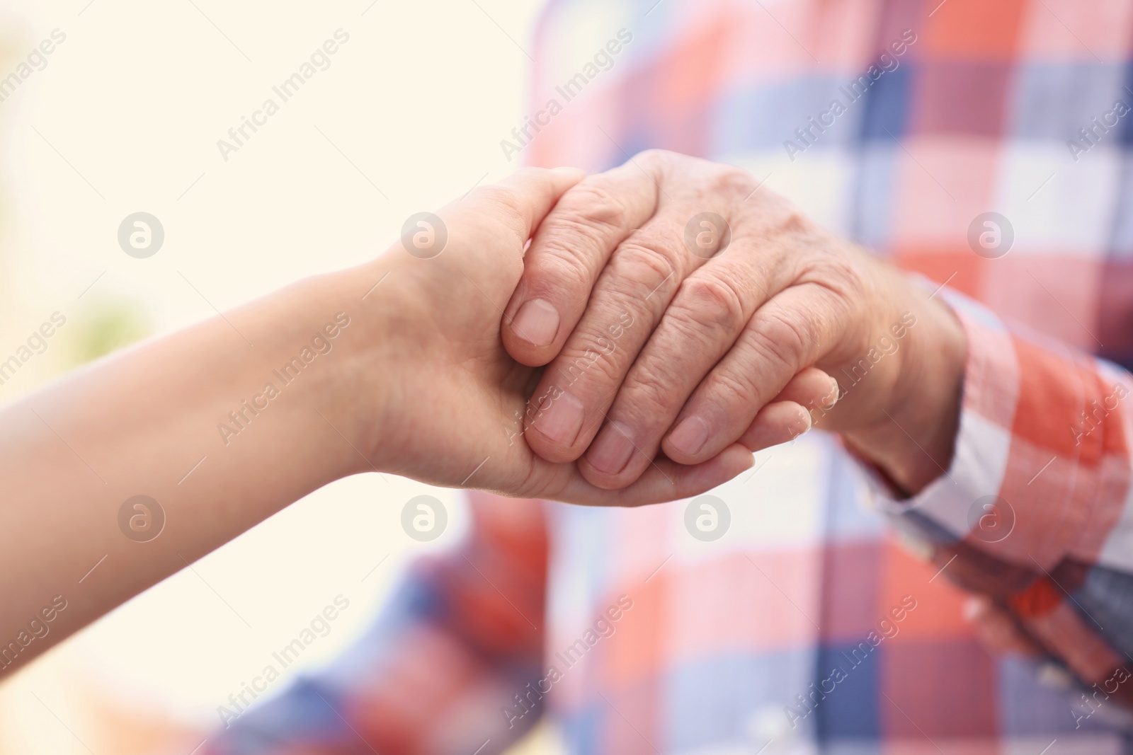 Photo of Young woman holding elderly man hand on blurred background, closeup. Help service