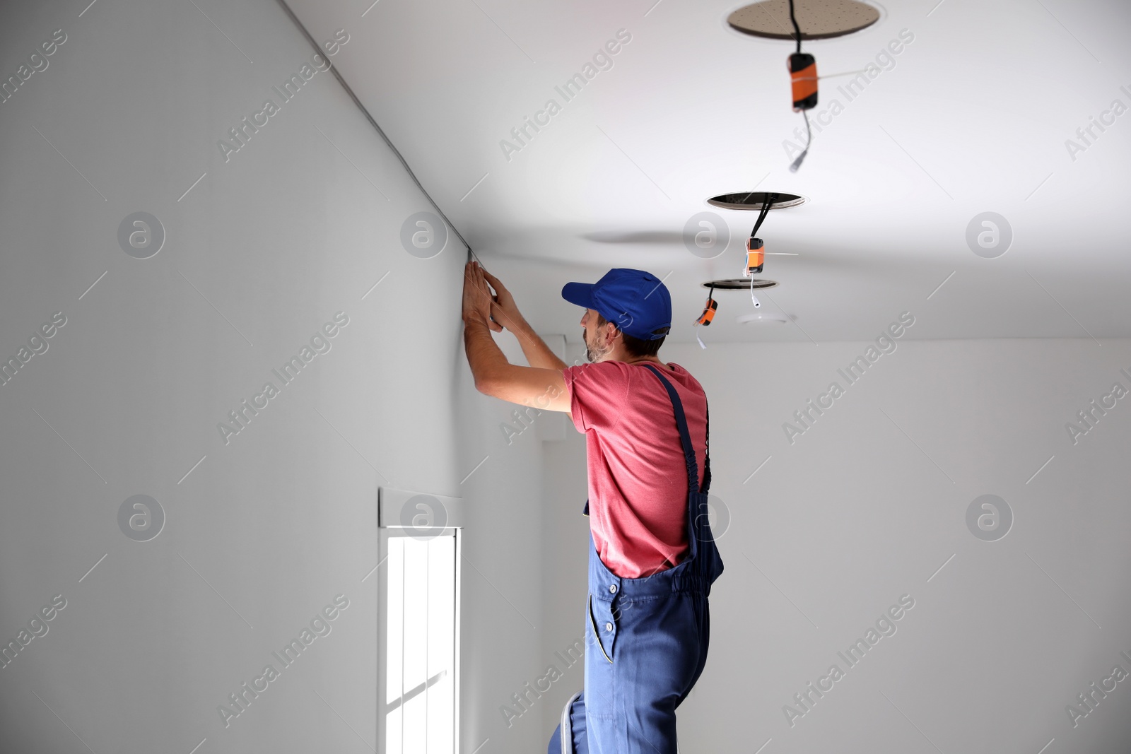 Photo of Worker installing stretch ceiling in empty room