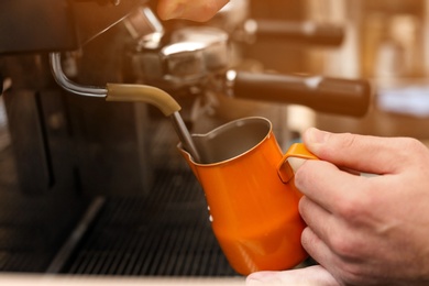 Photo of Male barista using coffee machine for steaming milk in pitcher, closeup