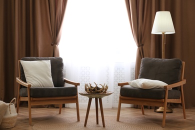 Comfortable armchairs near window with stylish curtains in living room. Interior design