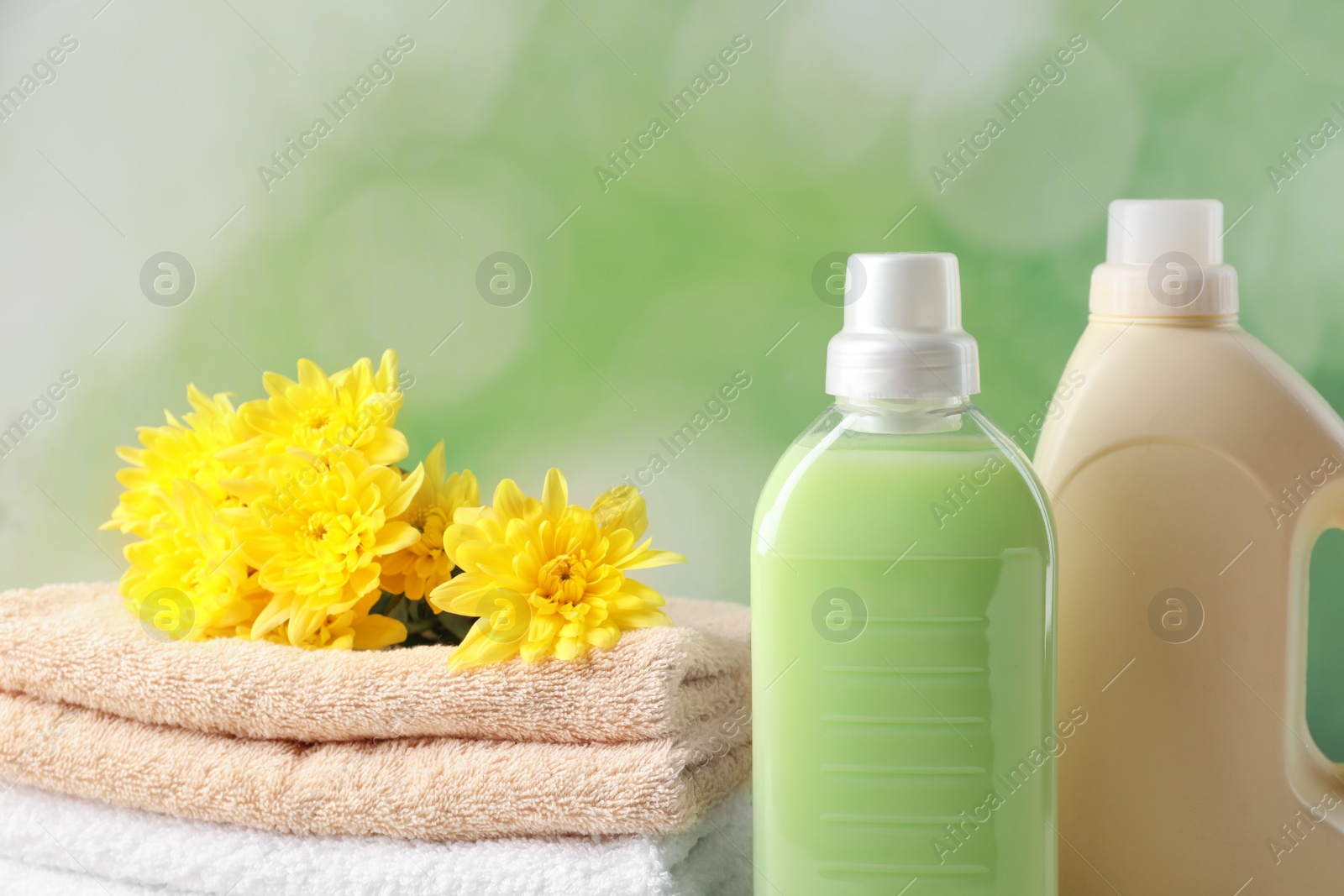 Photo of Bottles of laundry detergents, towels and beautiful flowers on blurred background, closeup