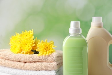Photo of Bottles of laundry detergents, towels and beautiful flowers on blurred background, closeup