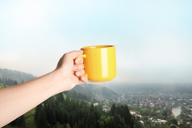 Image of Closeness to nature. Woman holding cup in mountains, closeup