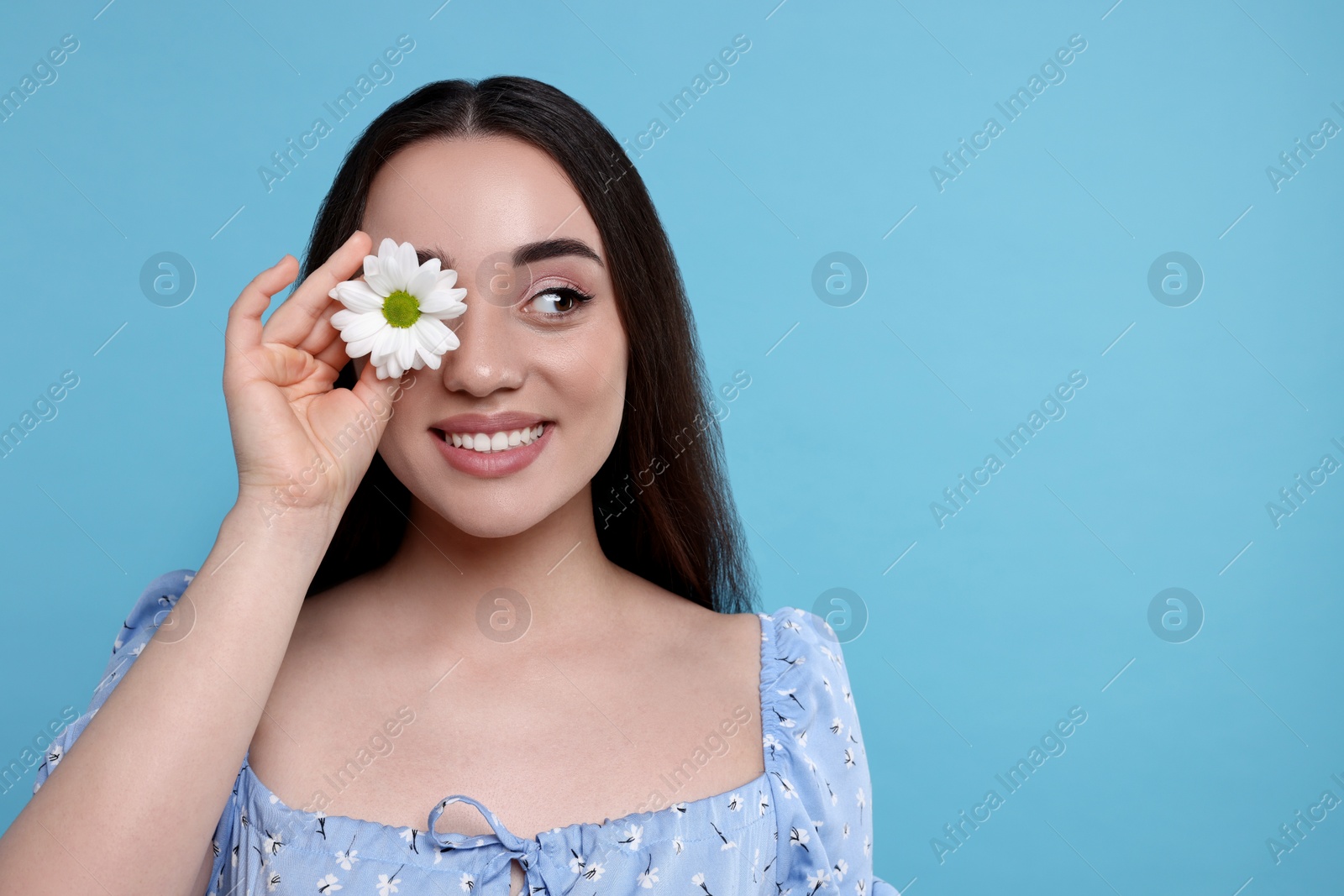 Photo of Beautiful woman with spring flower in hand on light blue background, space for text