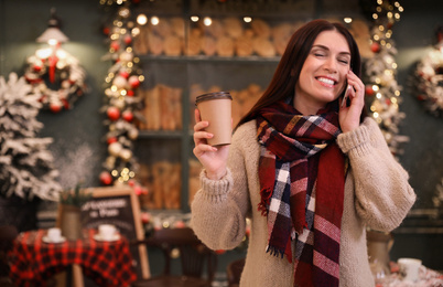 Photo of Beautiful woman with cup of coffee talking on mobile phone in decorated cafe. Christmas celebration