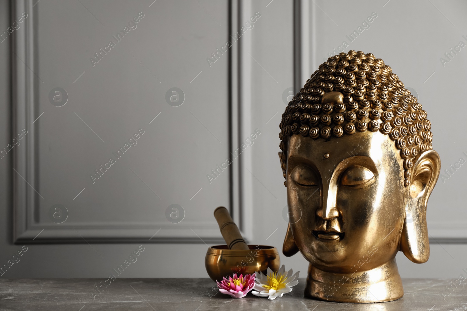 Photo of Buddha statue, singing bowl and lotus flowers on grey table. Space for text