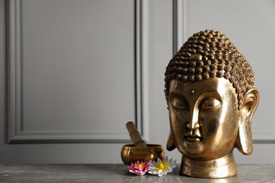 Photo of Buddha statue, singing bowl and lotus flowers on grey table. Space for text