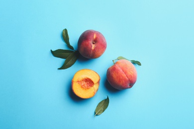 Photo of Fresh ripe peaches and green leaves on light blue background, flat lay