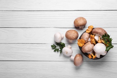 Bowl with different mushrooms and parsley on white wooden table, flat lay. Space for text